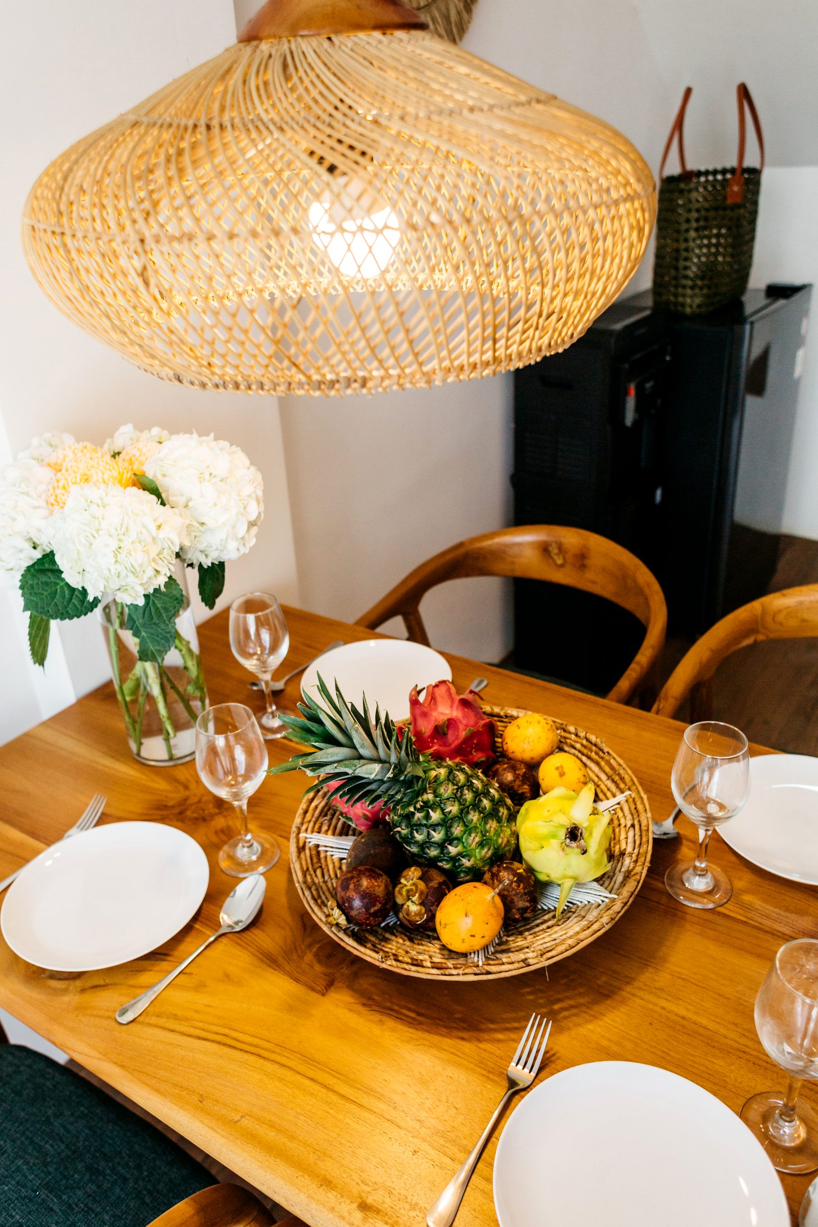 Styled dining table with tropical fruit and flowers under a rattan pendant — villa interior, Ubud Bali